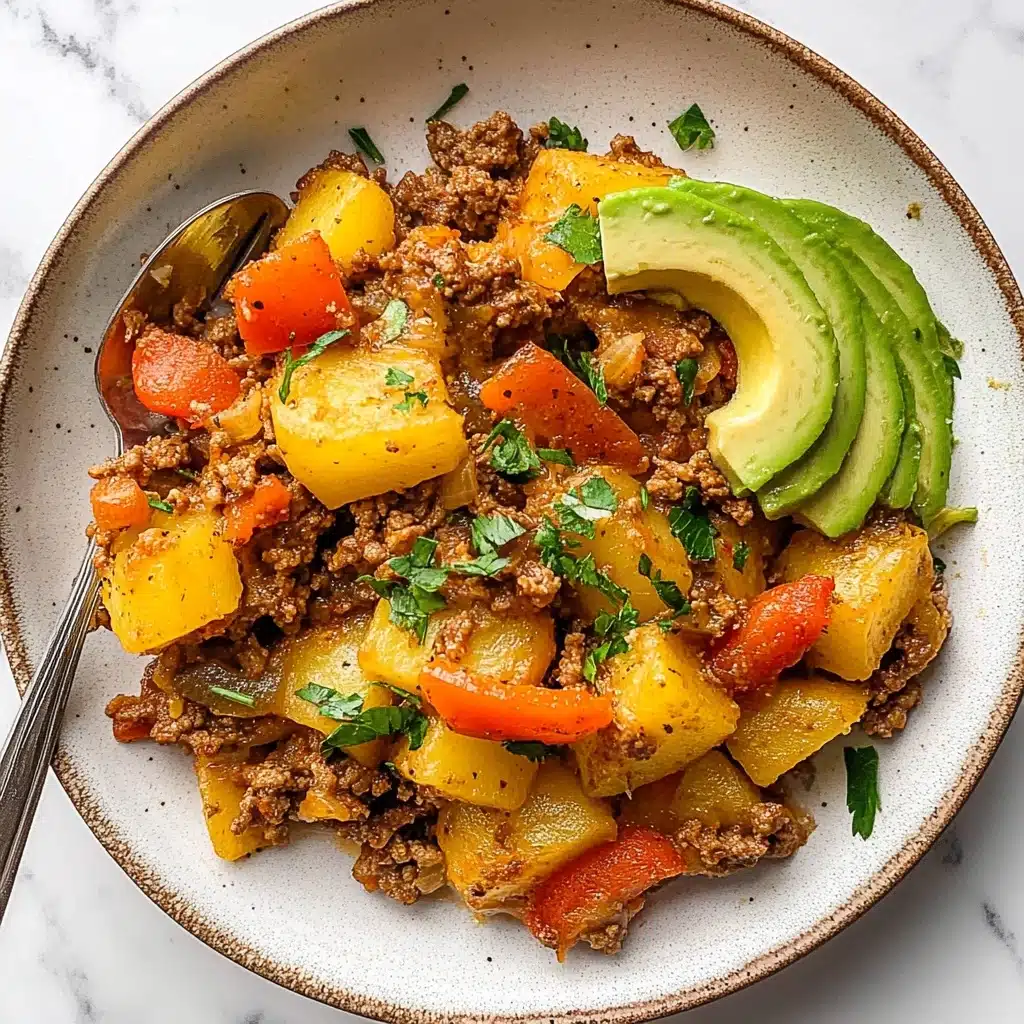 Mexican Ground Beef and Potato Skillet, Mexican Ground Beef Skillet, Easy Mexican Beef and Potato Dinner, One-Pan Mexican Beef and Potatoes, Hearty Mexican Beef Skillet A round white plate holds a colorful dish with three main layers. The bottom layer is a mix of browned ground meat and diced yellow potatoes, cooked with soft, translucent onion pieces and melted orange cheese scattered throughout. Mixed in this layer are bright red bell pepper chunks and green parsley leaves, adding color and freshness. On top to one side, thin slices of pale green avocado are neatly fanned out, garnished lightly with more green herbs. A silver spoon rests on the plate’s left edge, partly under the food. The plate sits on a white marbled surface.