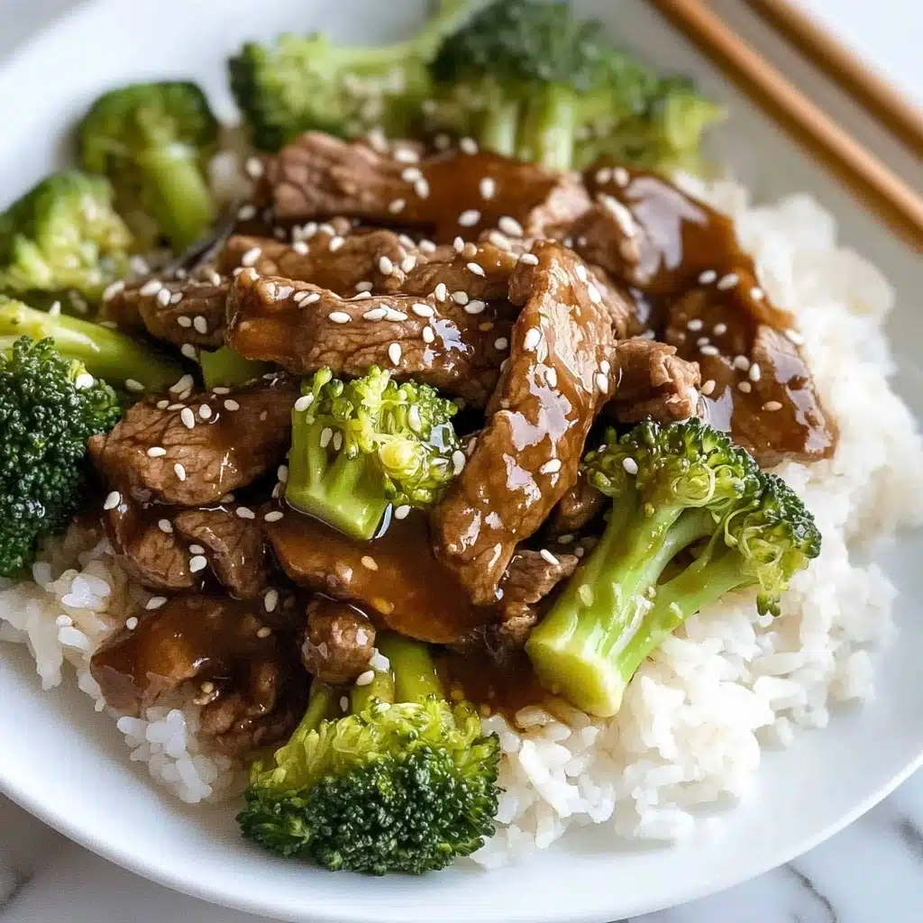 Chinese Beef and Broccoli, Chinese Beef and Broccoli recipe, homemade Chinese beef and broccoli, easy beef and broccoli stir-fry, takeout-style Chinese beef and broccoli A white plate holds a serving of white rice as the base layer, topped with bright green broccoli pieces and brown slices of beef. Both the beef and broccoli are coated in a shiny, thick brown sauce, sprinkled with small white sesame seeds. The broccoli pieces show a bumpy texture on top with smooth stems, and the beef slices have a slightly rough texture with a glossy finish from the sauce. The food is placed on a white marbled tabletop with wooden chopsticks resting on the edge of the plate.