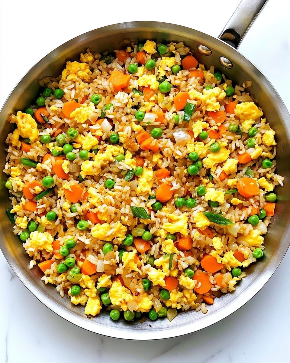 Easy Egg Fried Rice, quick egg fried rice, simple homemade fried rice, flavorful egg fried rice, beginner-friendly fried rice A close-up of a white bowl full of fried rice, showing a mix of light brown rice grains, bright yellow scrambled eggs, small green peas, chopped red bell peppers, and pieces of cooked onions. The bowl is held by a woman's hand using wooden chopsticks on the left side, picking up some rice. The background and surface are white with a marble texture, making the colors of the food pop. The dish looks fresh and colorful with a mix of soft and slightly crispy textures in the rice and vegetables.