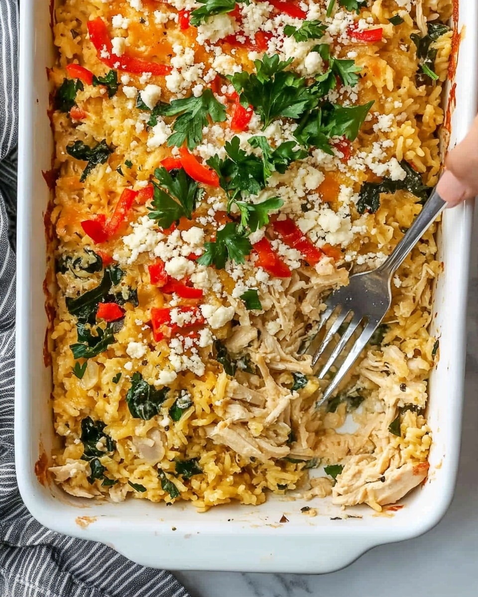 Greek Chicken Casserole with Orzo, Greek Chicken Bake with Feta and Spinach, Mediterranean Chicken Casserole, Easy Greek Chicken Meal, Cheesy Spinach Chicken Bake The image shows a white rectangular baking dish filled with a layered casserole. The base layer consists of shredded light beige chicken mixed with yellow cooked rice. Scattered throughout are bits of dark green leafy vegetables, finely chopped red bell peppers, and small pieces of caramelized purple onion. On top, there are white crumbles of cheese and sprigs of fresh green parsley. A silver fork is partially submerged in the casserole on the right side, with a woman's hand holding it. The dish is placed on a white marbled surface with a gray-striped cloth partially visible underneath one handle of the baking dish.