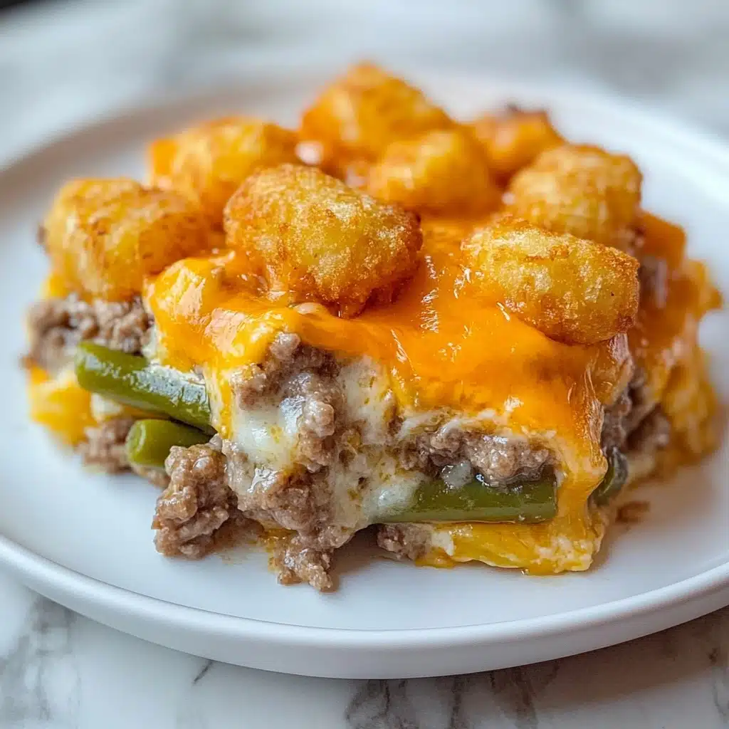 Tater Tot Casserole, easy tater tot casserole, cheesy tater tot bake, hearty dinner ideas, comfort food recipes The dish is made in three clear layers, all on a white plate on a white marbled surface. The bottom layer is a mix of cooked ground meat with diced onions, visible in a creamy white sauce with some melted cheddar cheese. The middle layer consists of green beans covered with melted cheddar cheese, adding a yellow-orange color in the middle. The top layer is made of golden brown, crispy tater tots, arranged neatly and evenly on top, some sitting on the cheesy middle layer. The cheese is melted and slightly stretching between the layers, giving a warm and tasty look.