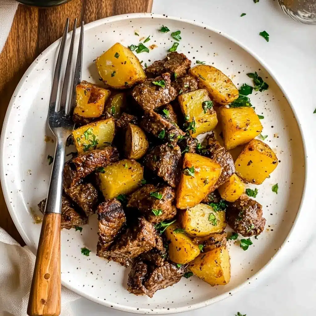 Garlic Butter Steak Bites and Potatoes, garlic butter steak recipe, easy steak dinner, quick potato dish, indulgent weeknight meal A white round plate holds a simple meal with two main layers: the first layer is golden yellow potato chunks with a slightly crispy texture, scattered around the plate, some showing slight browning edges; the second layer is browned beef pieces, tender and juicy looking, mixed evenly with the potatoes and sprinkled with fresh green herbs on top for color contrast. A fork and knife with wooden handles are placed on the left side of the plate, resting on a white marbled surface. Shadows and light suggest natural daylight.