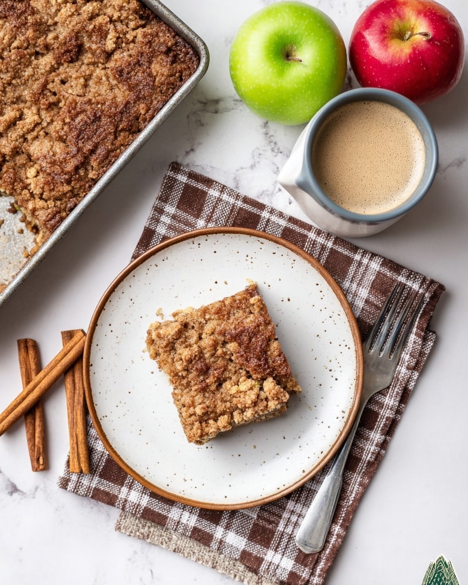 A crumbly brown cake square is placed on a round white speckled plate with a brown rim. The cake has a rough textured top that looks soft inside. A woman's hand with a silver fork is teasing into the side of the cake. In the background, a black rectangular pan filled with the same brown crumb cake is partially visible, slightly out of focus. To the left, there is a green apple resting next to a white and brown striped cloth on a white marbled surface. On the right side, a ceramic cup with a beige top and dark gray bottom sits near the plate. Photo taken with an iphone --ar 4:5 --v 7