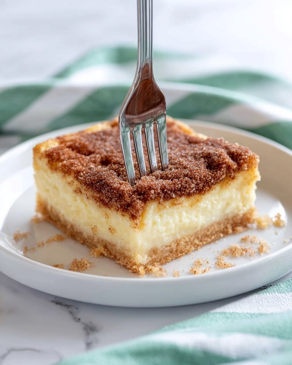The image shows a stack of three square dessert bars placed on a white marbled surface. Each bar has three layers: a golden-brown crispy bottom crust, a thick creamy pale yellow middle layer, and a top layer covered with a coarse, crumbly mixture of cinnamon and sugar, giving a rough texture and a rich brown color. The middle bar has a bite taken out, exposing the soft texture of the creamy middle layer and the crunchiness of the crust below. The cinnamon sugar on top appears uneven with some granules sparkling in the light. Photo taken with an iphone --ar 4:5 --v 7