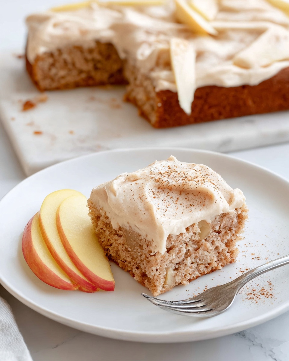 The image shows a rectangular cake covered with smooth light brown frosting, spread evenly on all sides. The cake sits on white parchment paper over a white marbled surface. On the top left corner and bottom right corner of the cake, there are small, decorative apple slices shaped like roses, showing soft yellow and pale red shades. Around the cake, there are a few cut pieces, also frosted with the same light brown cream and sprinkled lightly with cinnamon. In the lower left corner, a white plate holds a slice of the cake with an apple rose beside it, next to a silver fork. The overall scene is bright and clean with soft natural lighting, photo taken with an iphone --ar 4:5 --v 7