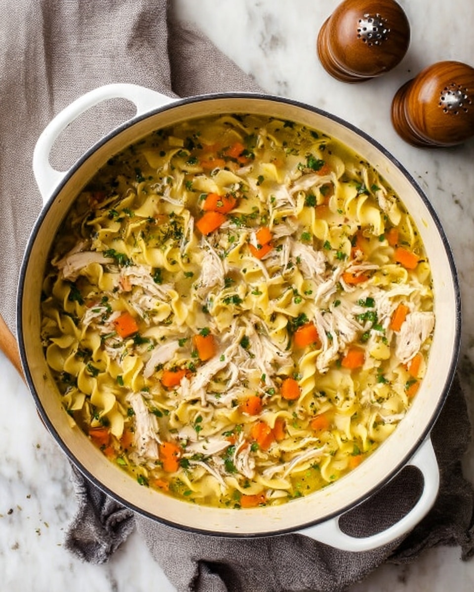 The image shows a bowl of chicken noodle soup placed on a white marbled surface. The soup has three main layers visible: the bottom layer is a clear light broth, the middle layer contains wide egg noodles that are pale yellow and curly, and the top layer includes small, diced orange carrots, shredded white chicken pieces, and small chopped green celery, all sprinkled lightly with finely chopped green herbs. The bowl is white and textured, and a metal spoon is resting inside the soup. Around the bowl, there are other bowls of the same soup, as well as glasses of water with lemon slices, all on the white marbled surface. photo taken with an iphone --ar 4:5 --v 7