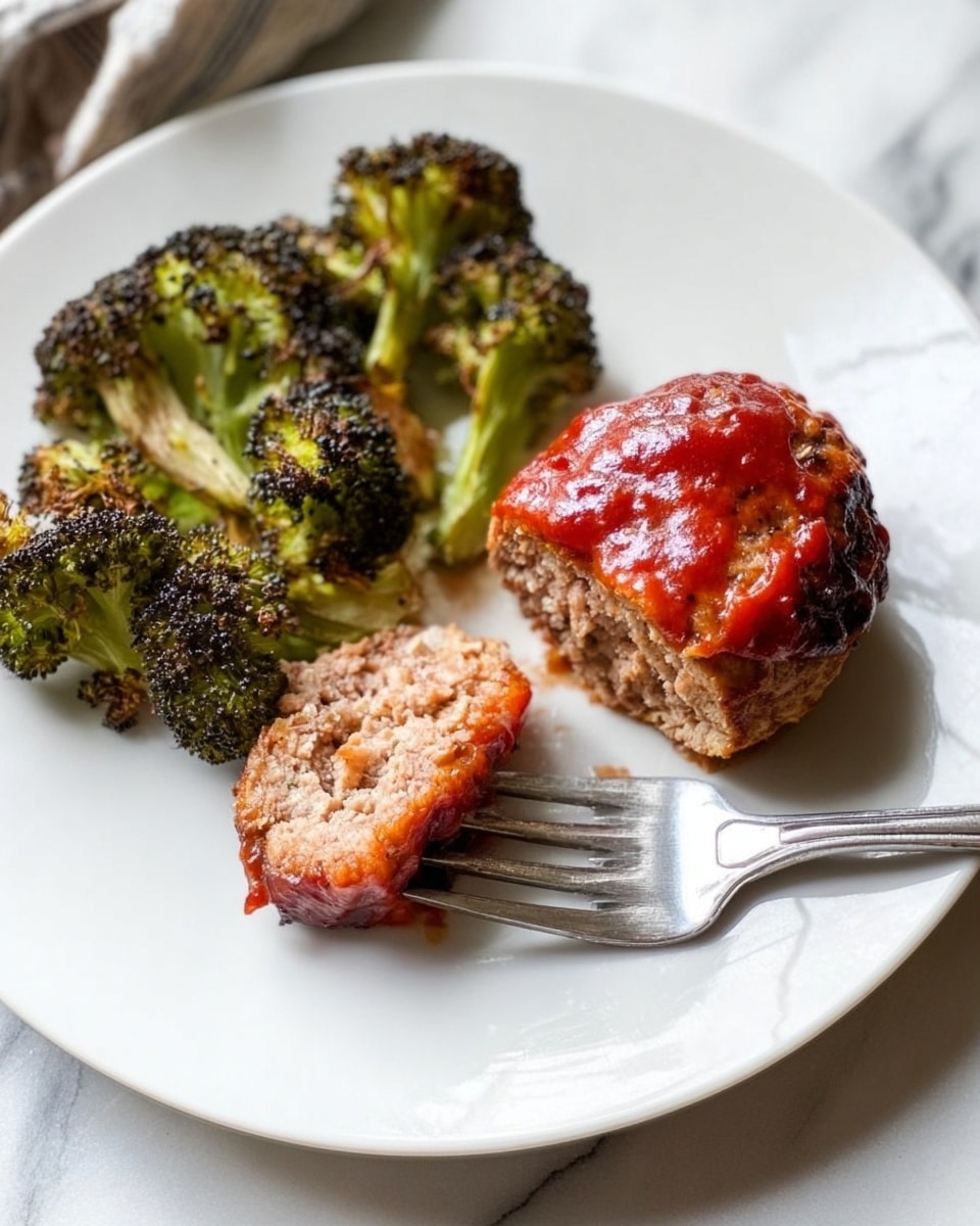 The image shows four round cooked meatballs covered with a shiny red sauce, placed on a sheet of foil. Above the meatballs, there are roasted broccoli pieces with a slightly browned, crispy texture and green color. The foil reflects some light and rests on a surface with a white marbled texture. The composition looks neat with the food spread out evenly. photo taken with an iphone --ar 4:5 --v 7
