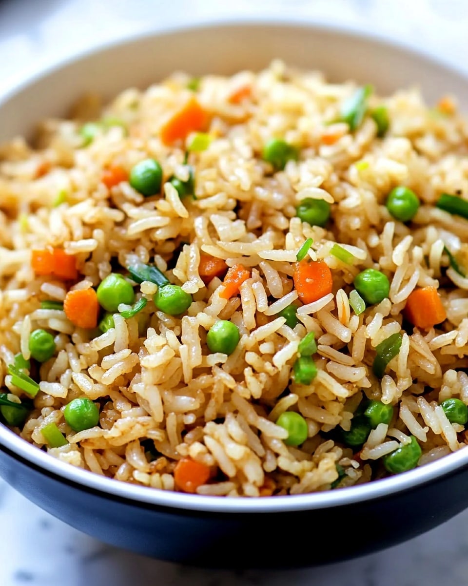 A close-up view of a bowl filled with fried rice showing a mix of long grains of light golden brown rice scattered with small bright green sliced spring onions and tiny pieces of orange carrot. The rice looks fluffy with a slight shine and is mixed evenly with the vegetables, all inside a white bowl. The background shows a soft focus and a white marbled surface beneath the bowl. photo taken with an iphone --ar 4:5 --v 6.1