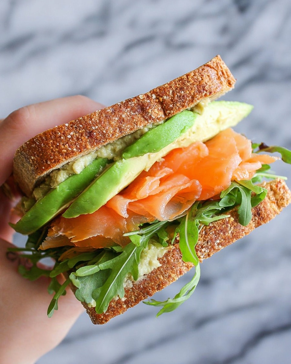 The image shows a sandwich with two thick slices of grilled bread with light brown grill marks on top and bottom. Inside, there are several layers starting with dark green leafy lettuce, followed by thin slices of light green cucumber, then folds of orange-pink smoked salmon, topped with green slices of avocado and dotted with white creamy sauce with herbs on top. The sandwich sits on a white marbled surface with a white cloth nearby. photo taken with an iphone --ar 4:5 --v 7