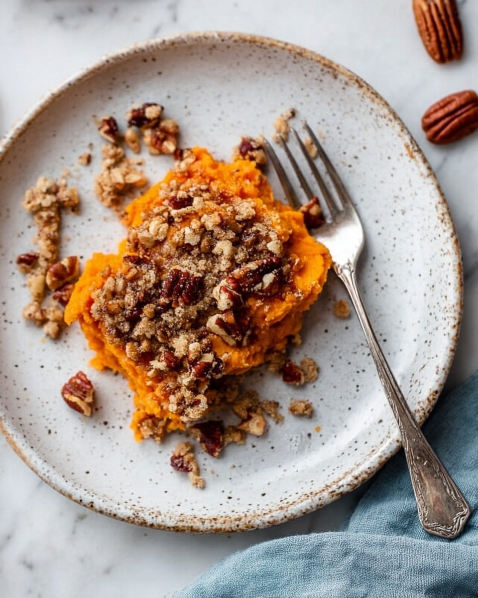 The image shows a white speckled ceramic plate with a serving of bright orange mashed sweet potato layered with a crumbly topping made of oats and chopped pecans scattered over it. The sweet potato layer is smooth with a slightly mashed texture while the topping adds a crunchy look with rough oat flakes and darker brown pecans. A silver fork rests partially under the food on the right side of the plate. Around the plate on the white marbled surface, there are a few extra pecan pieces and a soft blue cloth in the corner. Photo taken with an iphone --ar 4:5 --v 7