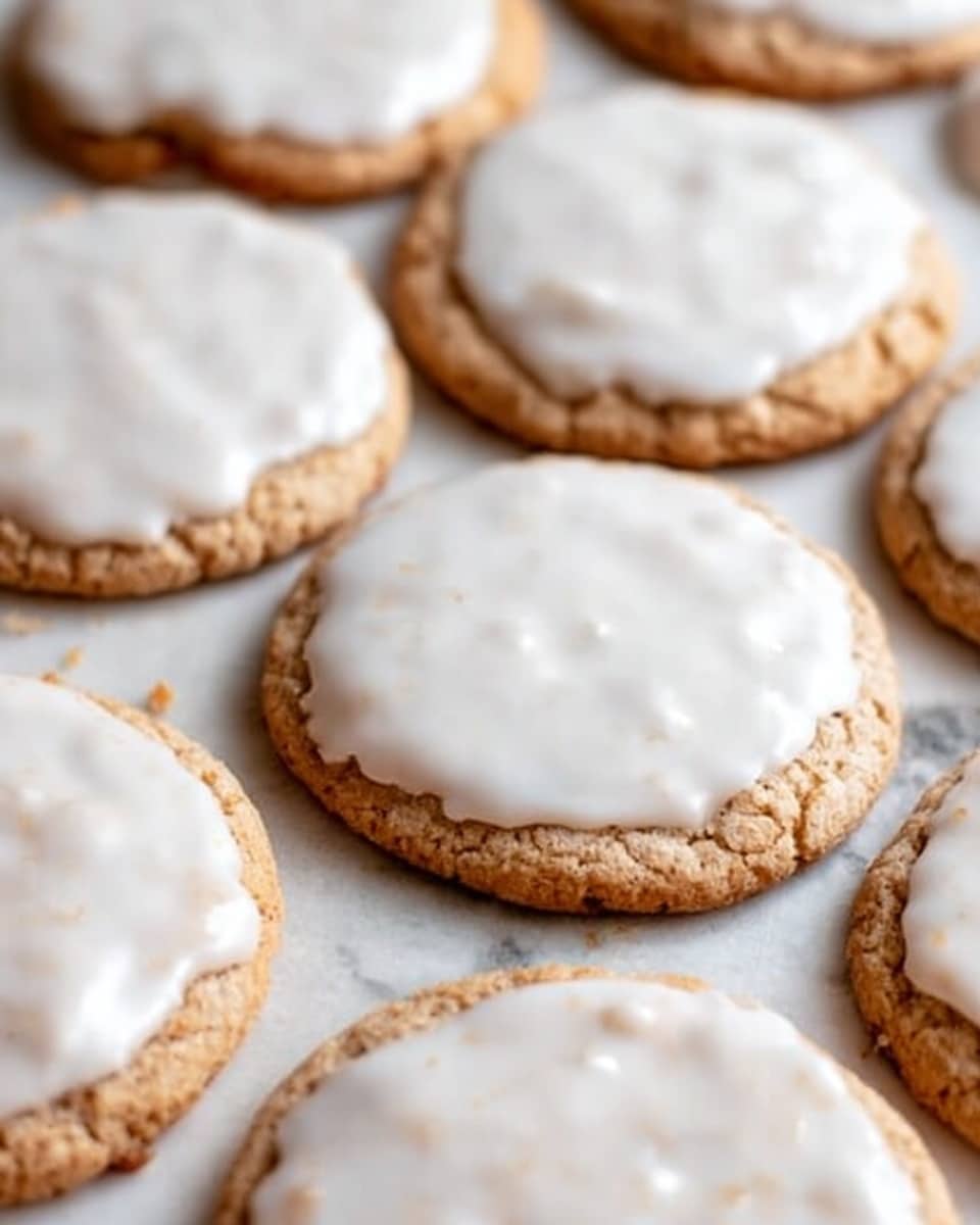 A white plate full of round cookies with a light brown base and a thick layer of white icing on the top, some cookies showing a slightly rough texture under the icing, all neatly stacked on a white cloth with gentle folds on a white marbled surface, in the background a glass jar of milk and a metal cup filled with oatmeal, a wooden spoon and some scattered oats placed nearby, photo taken with an iphone --ar 4:5 --v 7