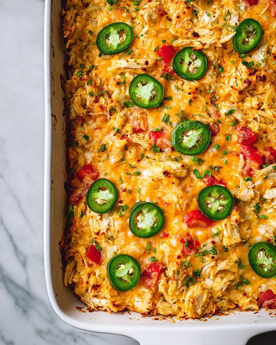 The image shows a white rectangular baking dish filled with a layered rice casserole. The top layer is golden and lightly crispy, made up of shredded cheese melted over cooked rice mixed with small red tomato pieces and tiny green herbs or scallions. There are round slices of fresh green jalapeño peppers scattered evenly across the surface. Beneath the cheese and rice, there are visible chunks of shredded meat and bits of onions mixed in. The edges of the casserole near the dish show some browned, crispy spots. The dish is placed on a white marbled surface. photo taken with an iphone --ar 4:5 --v 7