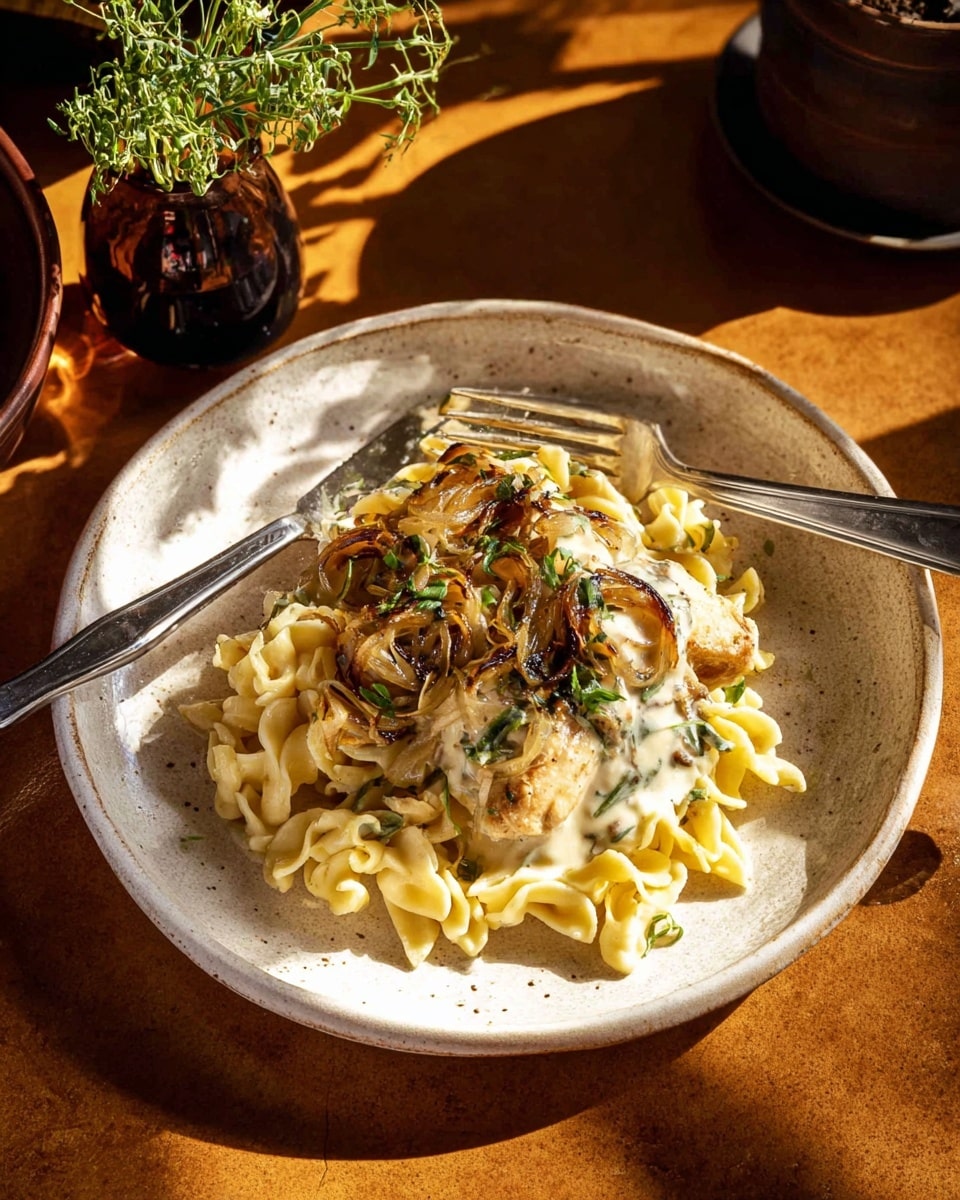 A white speckled round plate holds a dish with three main layers: at the bottom, soft, ruffled noodles in a pale yellow color form a dense base; on top of the noodles, there are thin caramelized onion slices that are golden brown with some darker edges; above these, a large piece of browned chicken sits in the center, covered partially by a creamy white sauce that drapes over parts of the noodles and onions. Scattered fresh green herbs add small spots of color across the dish. Two metal forks rest on the plate, one partially inserted into the food. The plate is set on a brown surface with warm sunlight casting soft shadows. In the background, a small glass vase with green leaves and a dark brown pot are seen. Photo taken with an iphone --ar 4:5 --v 7