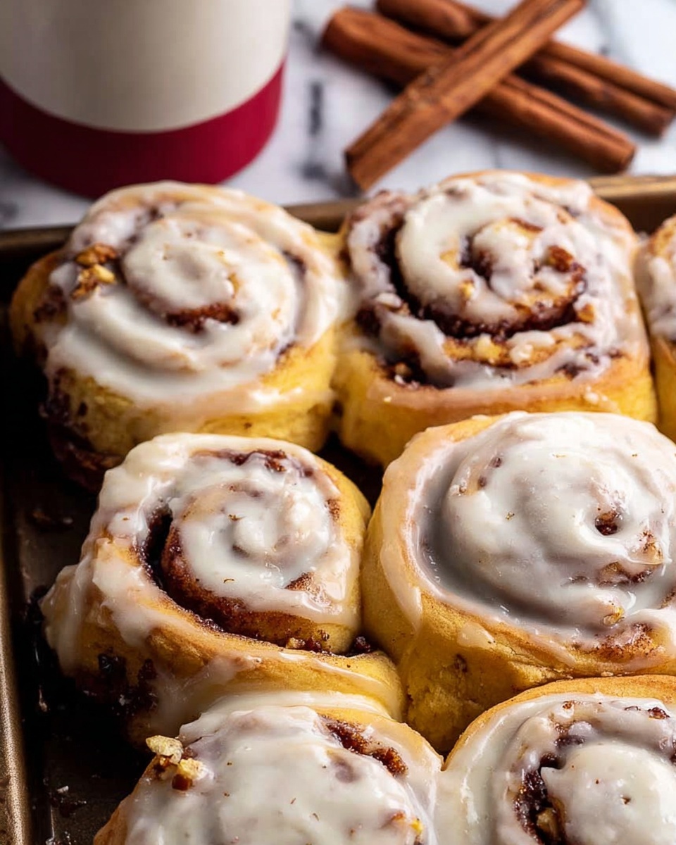 The image shows a close-up of six cinnamon rolls placed tightly together on a baking tray. Each roll has three visible spiral layers: a golden brown dough base with swirls of dark brown cinnamon filling and chopped nuts inside. The top layer is thick and creamy white icing, generously covering each roll unevenly, with some small specks visible in the icing. In the background, there are cinnamon sticks and a white cup with red on top, all set on a white marbled surface. photo taken with an iphone --ar 4:5 --v 7