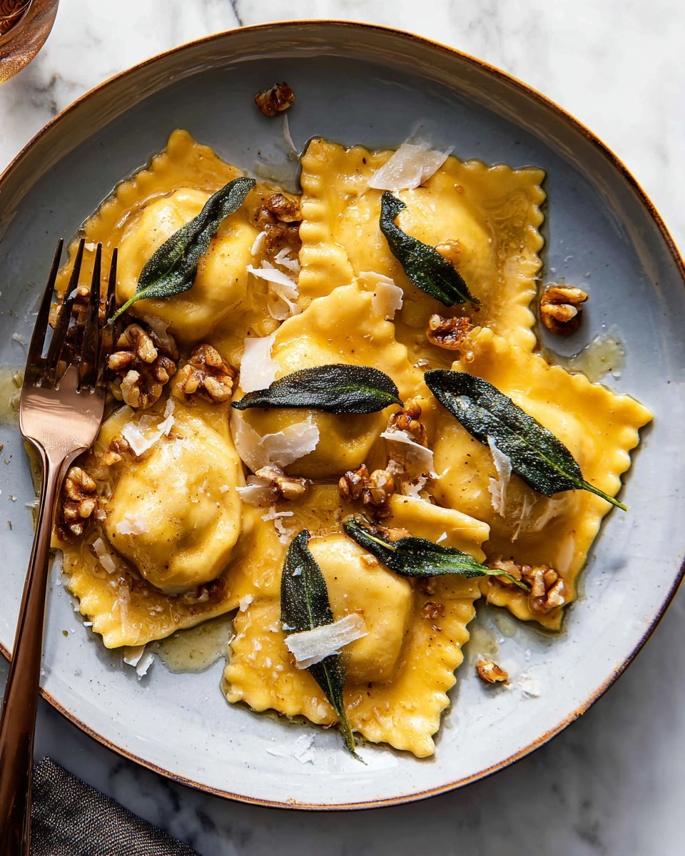 A white plate holds six large, golden-yellow ravioli pieces with slightly crimped edges, each topped with crispy dark green sage leaves. Scattered among the ravioli are small clusters of light brown walnut pieces and thin, irregular white shavings of cheese. A shiny bronze fork rests on the left side of the plate, slightly touching the food. The background shows a white marbled texture beneath the plate. photo taken with an iphone --ar 4:5 --v 7