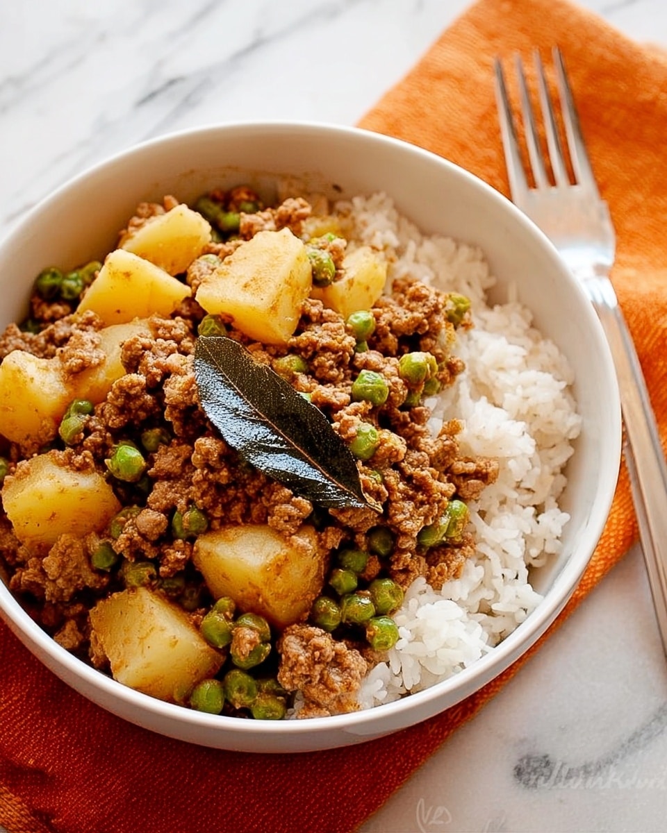 A white round plate filled with a base layer of fluffy white rice covering the whole plate's bottom, topped with a second layer of cooked ground meat mixed with small green peas and orange chunks of vegetables, all coated in a light brown sauce; a silver spoon rests inside the plate on the left side, touching both the rice and topping; the plate sits on a white marbled surface with a blue and white striped cloth napkin partially visible near the bottom right corner, photo taken with an iphone --ar 4:5 --v 7