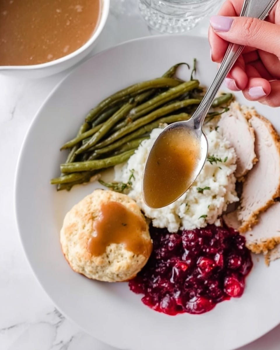 The image shows a white plate with three sections of food on a white marbled surface. There is a mound of white rice in the center of the plate with brown gravy poured over the top. To the left of the rice, there is a serving of green beans, and to the right, there are sliced pieces of roasted meat with red cranberry sauce on top. In the background, there is a white bowl filled with brown gravy, and a small white flower decorates the scene. Photo taken with an iphone --ar 4:5 --v 7