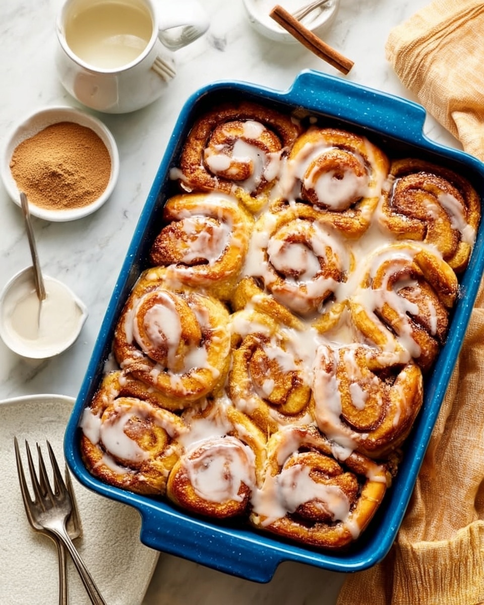 A deep blue baking dish filled with a thick layer of golden brown cinnamon rolls arranged closely in a single layer. Each roll shows swirls of light dough and darker cinnamon filling, with a shiny glaze coating the tops. One large cinnamon roll piece is being lifted by a silver spatula, showing its soft, fluffy texture and spiral layers inside. The dish is on a white marbled surface with a soft cloth nearby, and a woman's hand holding the spatula is partially visible. photo taken with an iphone --ar 4:5 --v 7