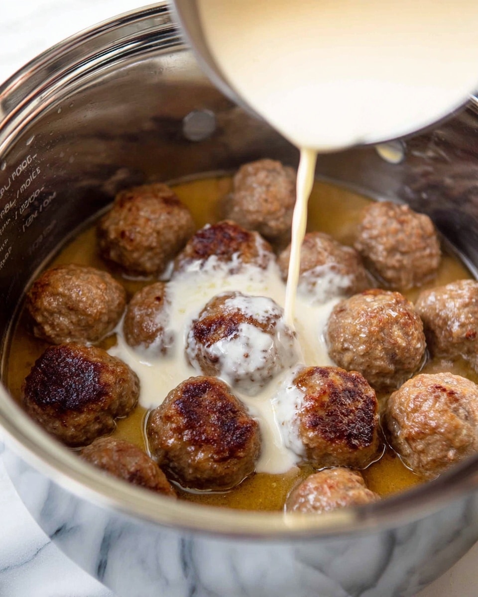 A white bowl filled with yellow egg noodles at the bottom topped with about ten light brown meatballs covered in a creamy beige sauce with small black specks. The meatballs have browned spots and appear soft and moist. Fresh green herbs are sprinkled on top of the meatballs for a pop of color. The bowl is sitting on a white napkin against a white marbled surface. photo taken with an iphone --ar 4:5 --v 7