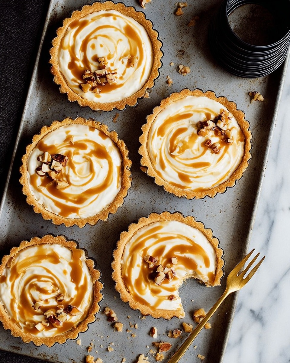 Five small tarts with golden edges are placed on a grey baking tray on a white marbled surface. Each tart has a creamy white filling swirled with caramel-colored sauce in smooth patterns. Small pieces of chopped nuts are scattered on top of the filling and around the tray. One tart has a bite taken out of it, showing a smooth filling inside. A small golden fork lies near the bitten tart. Near the top right corner, there are two black tart rings stacked together. photo taken with an iphone --ar 4:5 --v 7
