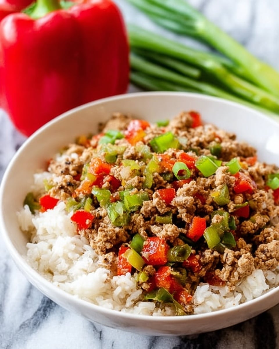 The image shows two white bowls on a white marbled surface, each filled with a colorful dish. The bottom layer in the closest bowl is white cauliflower rice, topped with finely shredded yellow cheese scattered unevenly. On top is a mix of cooked ground meat and diced red and yellow bell peppers, along with bits of onion, all mixed with herbs and spices giving a warm, textured look. Bright green parsley leaves rest on top as a garnish. In the background, another bowl contains the same dish, slightly out of focus, with a pair of salt and pepper shakers and some green plants around. A striped cloth is partially visible near the front, and some loose shredded cheese lies on the white marbled surface near a silver fork. Photo taken with an iphone --ar 4:5 --v 7