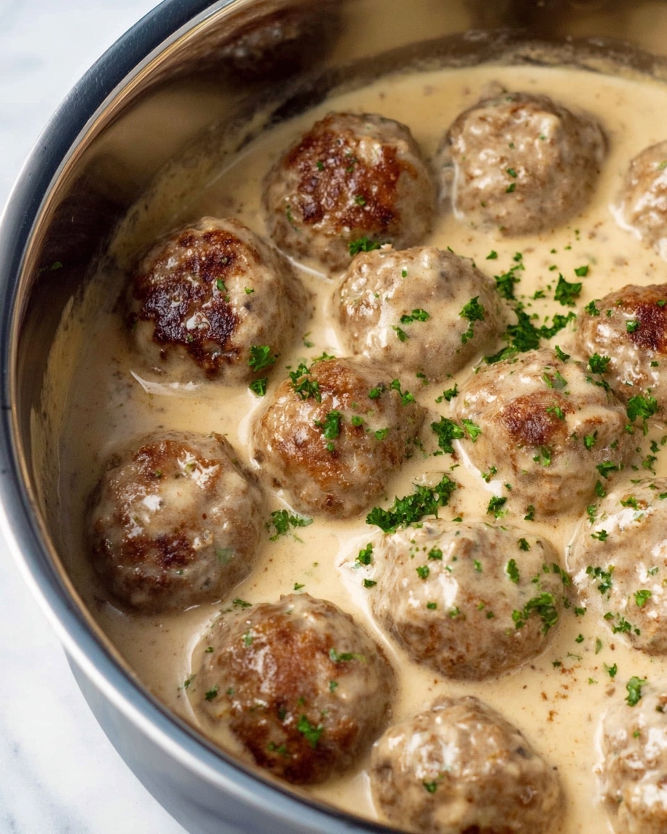 Inside a silver metal pot, there are about twelve brown meatballs, some with a browned crust on top and some lighter colored. The meatballs sit in a thin brown sauce at the bottom of the pot. A silver measuring cup is pouring a thick white cream sauce over the center meatballs, partially covering their tops. The pot has measurement marks visible on the side. The background surface is white marble. The scene looks close-up and bright. Photo taken with an iphone --ar 4:5 --v 7