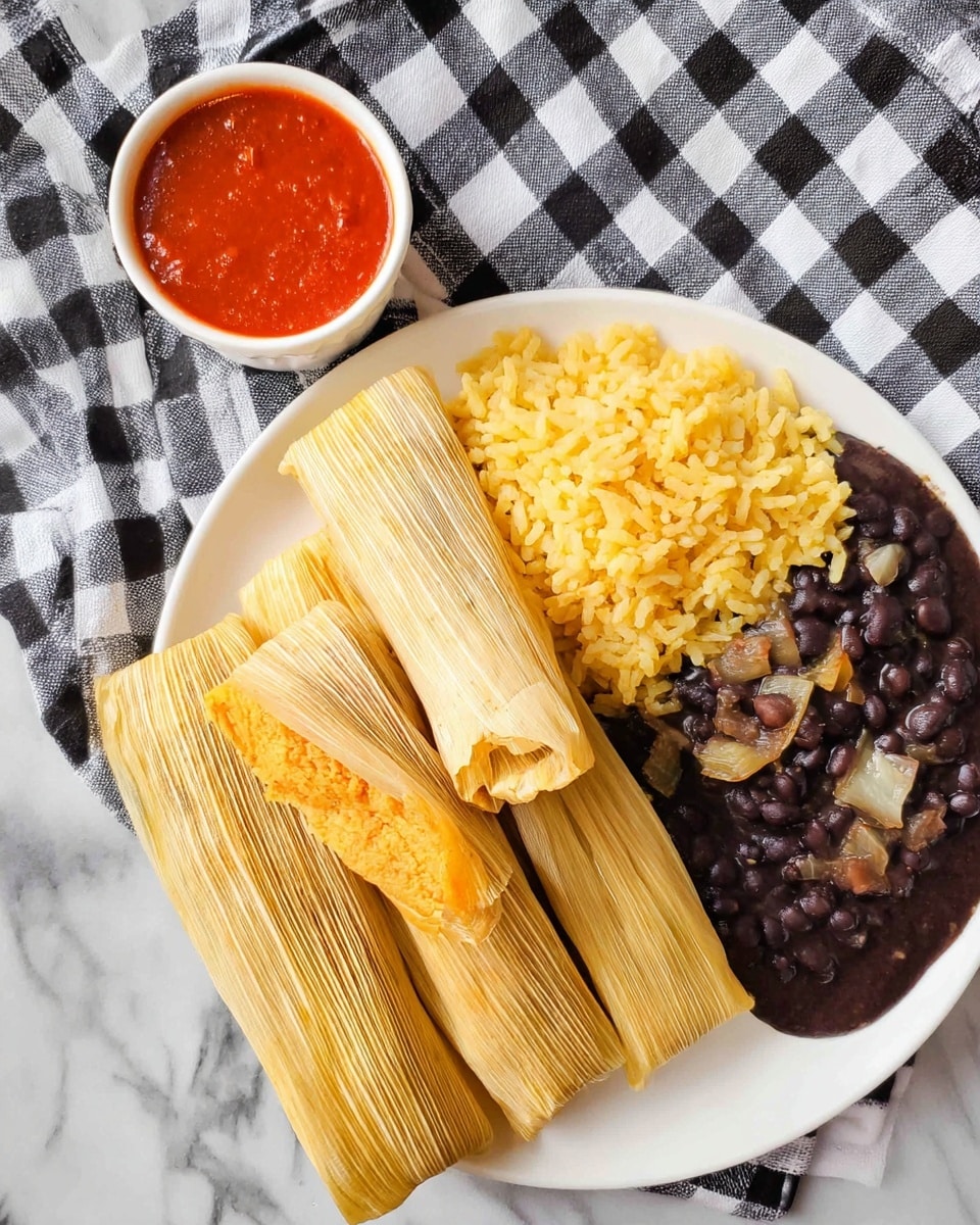 A single tamale is opened and resting in its light yellow corn husk, laid out on a white plate over a white marbled surface. The tamale filling is a soft, light brown masa layer, textured with small bits inside, and topped with a reddish-orange sauce that glistens gently. Beside it on the plate is another tamale still wrapped tightly in its corn husk and tied with a strip of husk. The setting is soft and backlit, showing the smooth and slightly shiny texture of the masa and the moist sauce on top. Photo taken with an iphone --ar 4:5 --v 7