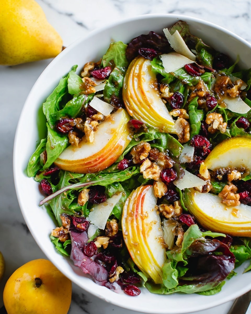 A colorful salad is shown in a white bowl on a white marbled surface. The salad has a base of fresh green and purple mixed leafy greens spread evenly across the bowl. Thin, light yellow pear slices with a hint of red are placed on top, layered among the leaves. Scattered throughout are small, rough-textured brown walnut pieces adding texture. Bright red dried cranberries add small pops of color, and thin shards of pale yellow cheese are spread irregularly over the salad. The whole dish is lightly coated with a shiny brown dressing, giving a slight gloss to the ingredients. A whole yellow pear sits next to the bowl, adding context to the fresh fruit used in the salad. Photo taken with an iphone --ar 4:5 --v 7