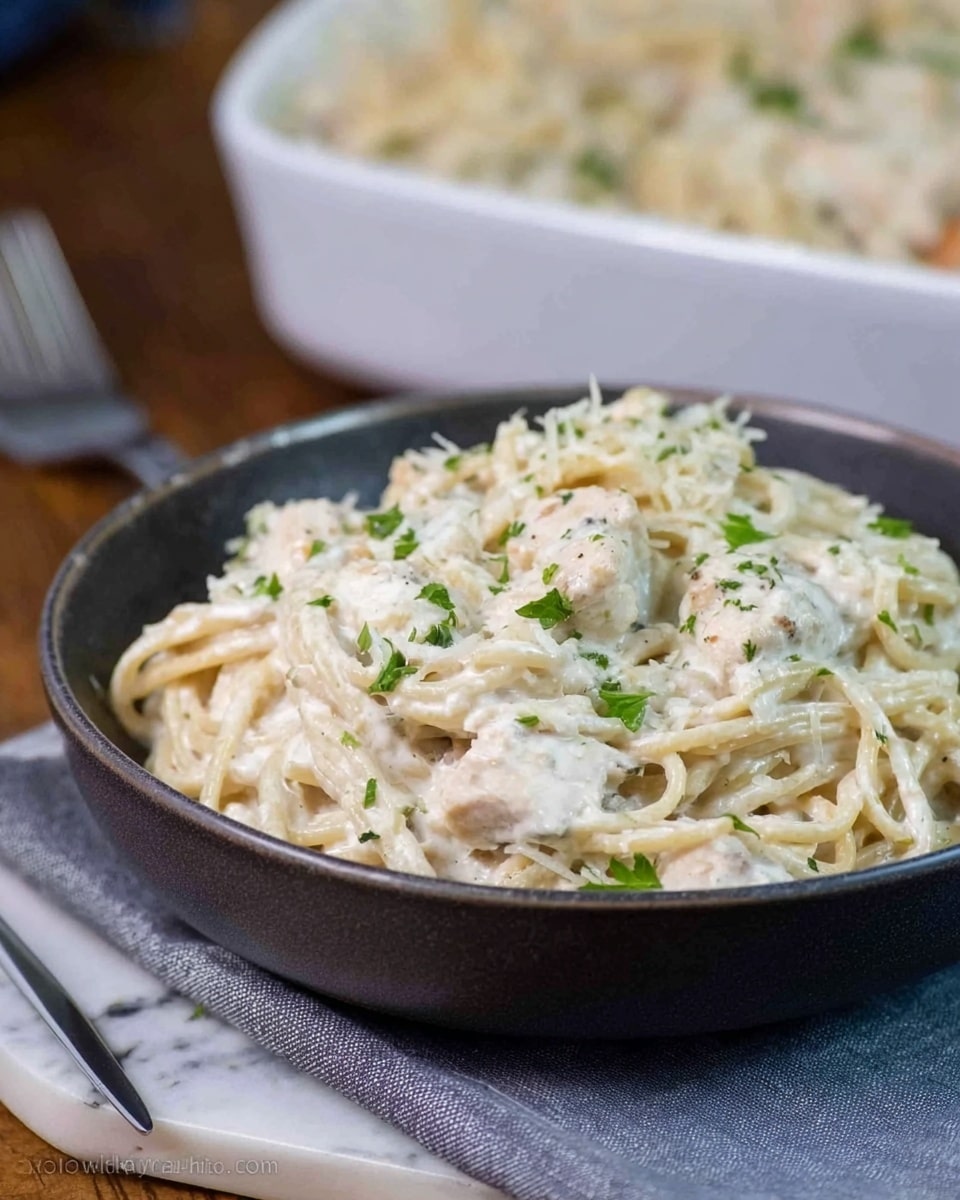 A close-up of a white plate with creamy pasta being lifted by a spoon. The dish has white cheese strings stretching from the plate to the spoon. The creamy sauce is light beige with chunks of mushrooms and pieces of white meat mixed in. There are small green herb pieces sprinkled on top and inside the sauce. The background and surface are white marbled. photo taken with an iphone --ar 4:5 --v 7