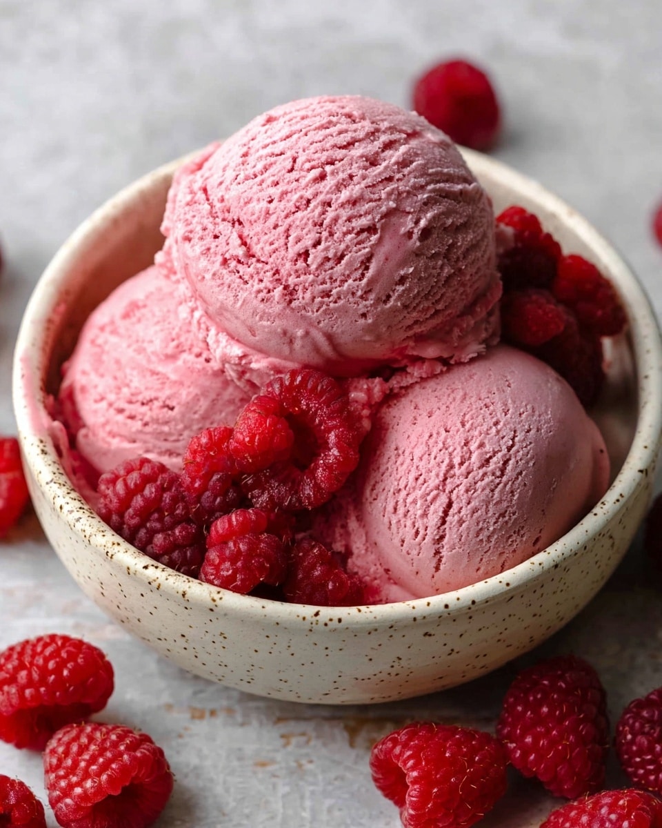 Three scoops of pink raspberry ice cream fill a white speckled bowl, with bright red fresh raspberries sprinkled on top and around the ice cream. The ice cream has a smooth but slightly textured surface, and the raspberries add a plump and shiny contrast. The bowl sits on a white marbled surface with several more raspberries scattered beside it. Photo taken with an iphone --ar 4:5 --v 7