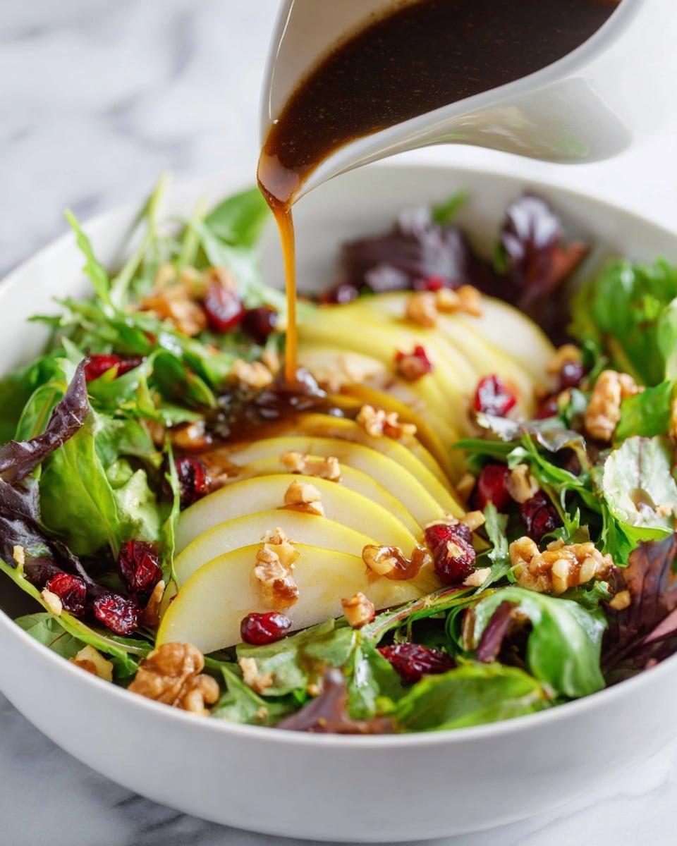 A white bowl filled with fresh green and purple leafy salad leaves forms the base layer, topped with thin yellowish slices of pear arranged evenly across the greens. Scattered on top are small clusters of chopped walnuts in light brown tones and dried red cranberries adding pops of color throughout. A dark brown dressing is being poured over the salad from a white pitcher, the liquid glistening as it falls onto the ingredients. The bowl sits on a white marbled surface, giving a clean and fresh look photo taken with an iphone --ar 4:5 --v 7