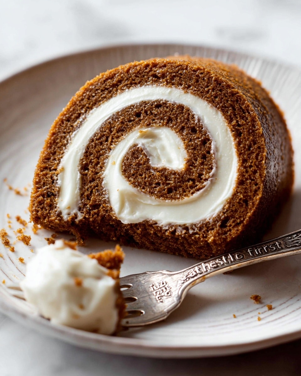 A close-up image of a single brown roll cake with one thick white cream layer spiraled inside, placed on a white plate with a slightly raised edge. The roll cake has a moist and soft texture with small visible crumbs. A silver fork with the words 