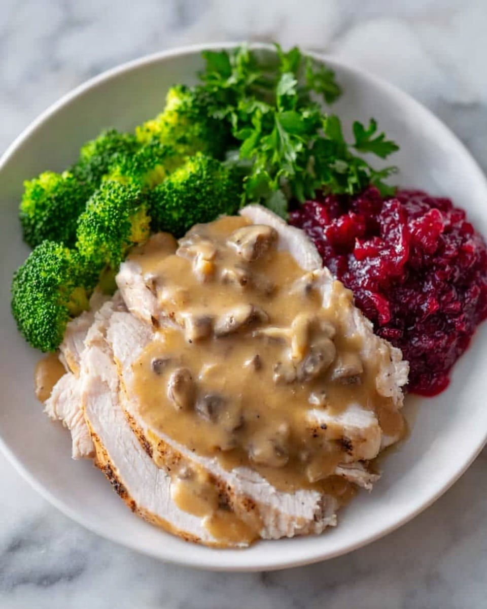 A white plate holds a meal with several layers: the bottom layer has pale, sliced cooked meat arranged in a slightly overlapping pattern in the center; over the meat is a thick, light brown gravy with visible small pieces of mushrooms spread evenly. To the left side of the plate, there are vibrant green steamed broccoli florets placed closely together. On the right side near the top, there is a deep red dollop of cranberry sauce with a textured surface. At the top right, fresh green parsley leaves add color. The plate sits on a white marbled surface. Photo taken with an iphone --ar 4:5 --v 7