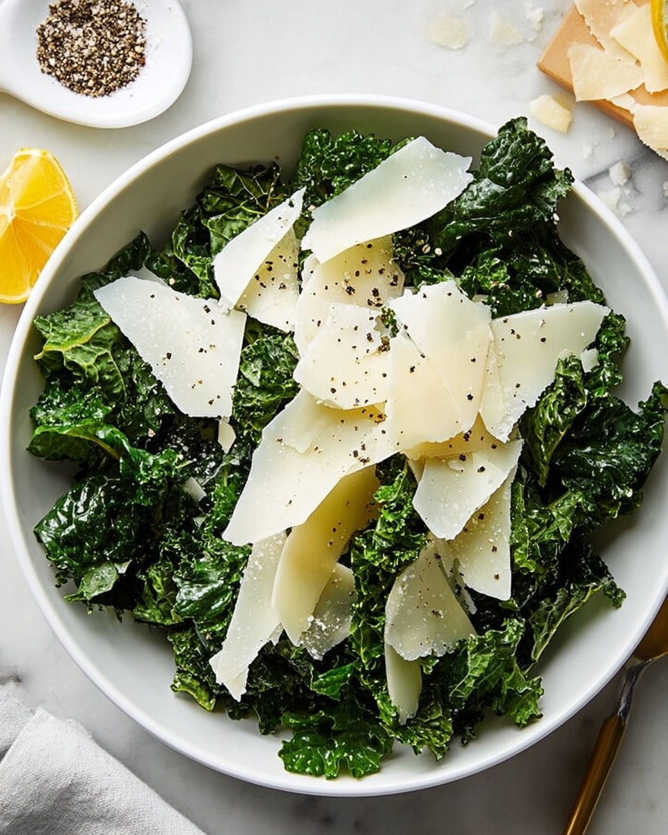 A white bowl filled with fresh dark green kale leaves, slightly curly and textured, forming the base layer. On top, light thin and irregular slices of pale yellow cheese are spread unevenly, some overlapping each other. Small black pepper grains are scattered across the cheese slices and kale leaves, adding tiny dark dots. The bowl sits on a white marbled surface, with a small white dish containing coarse salt and black pepper nearby, and a wedge of lemon partially visible on the left side. photo taken with an iphone --ar 4:5 --v 7
