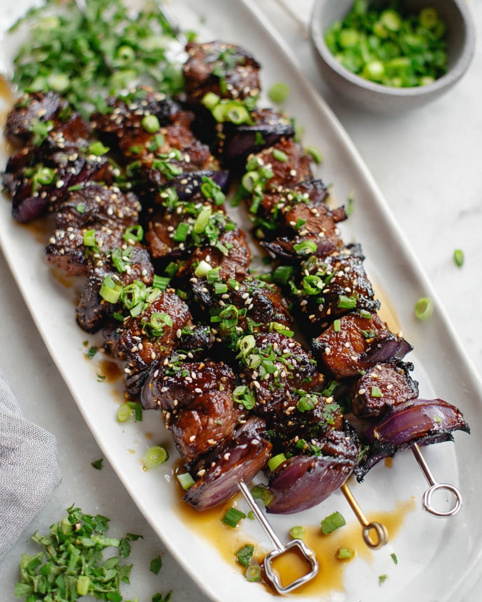 Four metal skewers lie across a long white plate, each threaded with dark brown grilled meat chunks that have charred edges, alternating with pieces of purple-red onion. The skewers are sprinkled with small green onion pieces and sesame seeds. To the side on the white marbled surface, there is a small metal cup filled with dark brown sauce with visible chili flakes and a clear glass of light yellow beer. Fresh green cilantro leaves are in the lower right corner, adding a fresh touch to the scene. Photo taken with an iphone --ar 4:5 --v 7