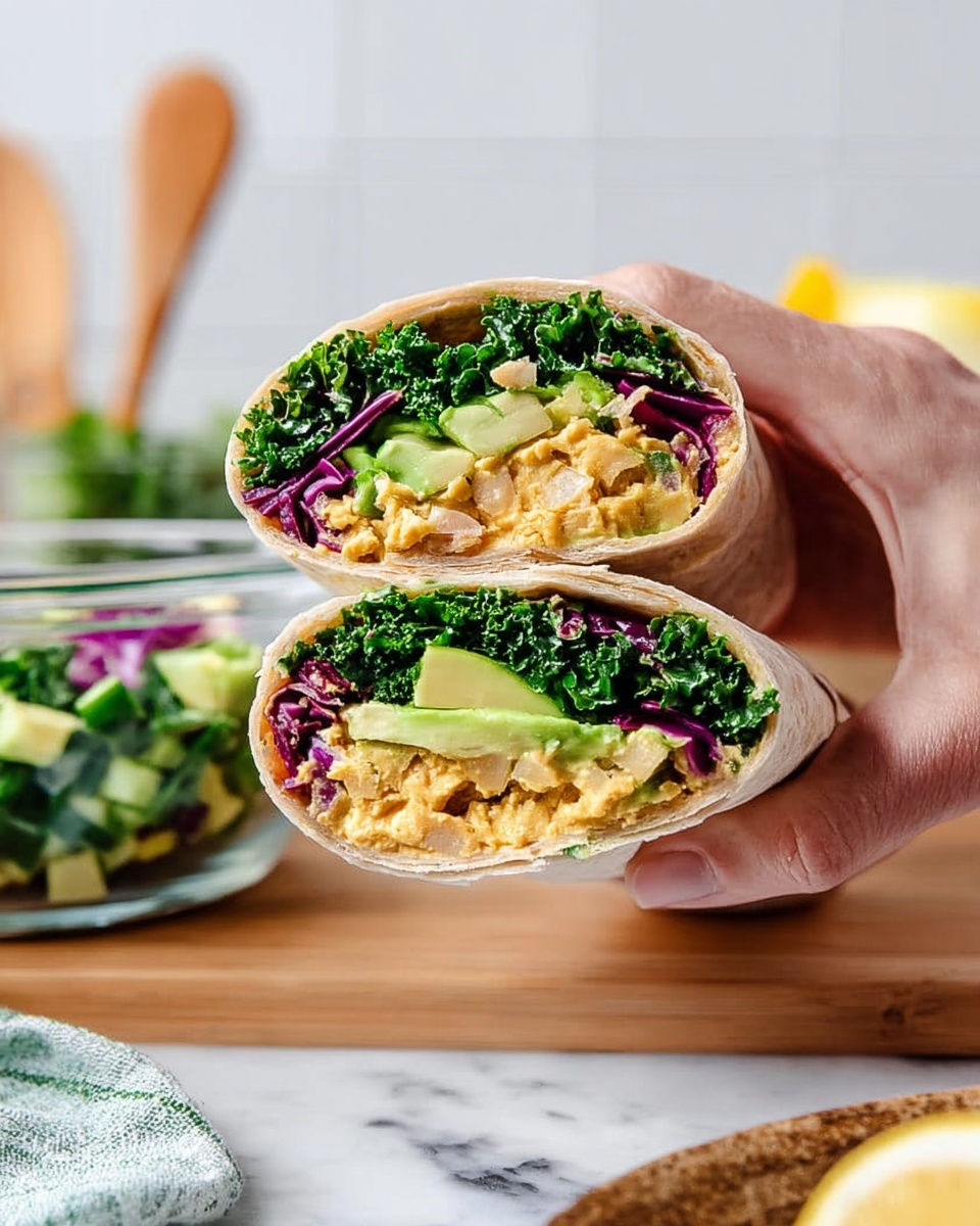 The image shows a wrap cut in half, held by a woman's hand, with two visible layers inside. The outer layer is a light beige soft tortilla. Inside, starting from the bottom, the first inner layer is a chunky, yellowish spread that looks like smashed chickpeas. Above it lies a layer of light green sliced avocado. The topmost layer is a mix of dark green leafy kale and bright purple-red cabbage, adding a fresh and colorful contrast. The wrap is set on a white marbled surface with a glass bowl filled with chopped green and purple vegetables in the background, along with a wooden spoon and a blurred lemon. Photo taken with an iphone --ar 4:5 --v 7