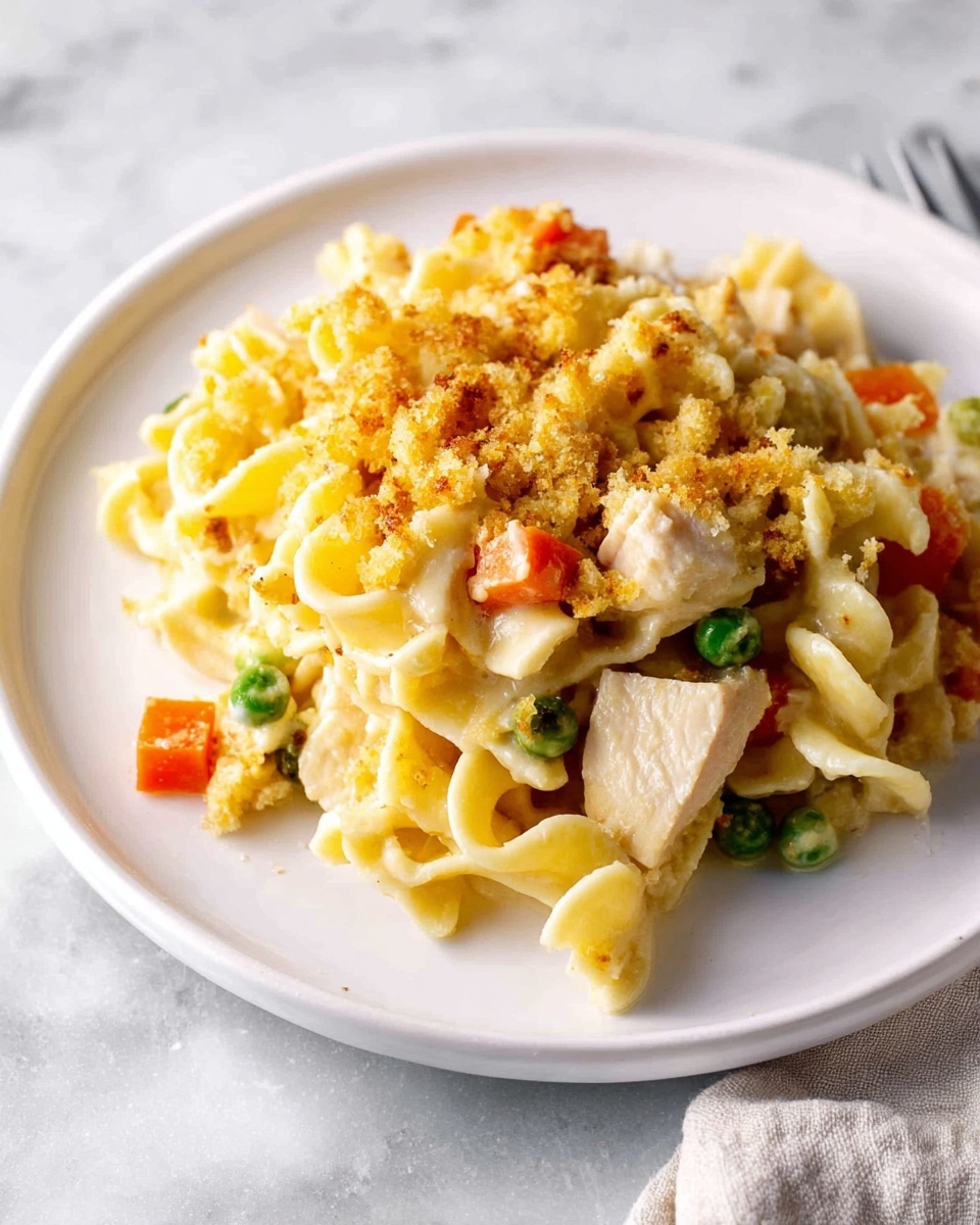 A large white rectangular baking dish filled with a baked noodle casserole. The dish has a visible layer of wide egg noodles mixed with small pieces of green beans, diced carrots, corn kernels, and chunks of white meat. On top, there is a golden-brown crumb topping that is unevenly spread, adding a crunchy texture. The noodles are creamy and slightly browned on the edges, hinting at melted cheese or sauce beneath. The baking dish sits on a white marbled surface. photo taken with an iphone --ar 4:5 --v 7