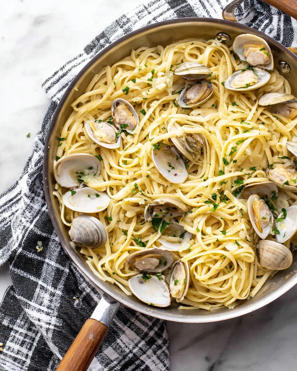 A large pan filled with light yellow pasta mixed with small pieces of garlic and small green parsley leaves scattered on top. Around the pasta, there are clam shells that are cream-colored with darker edges, some open to show the clam inside. The pan is silver and sits on a white marbled surface with a folded black and white checkered cloth underneath. The pasta is slightly twisted and intertwined, showing a smooth texture. photo taken with an iphone --ar 4:5 --v 7