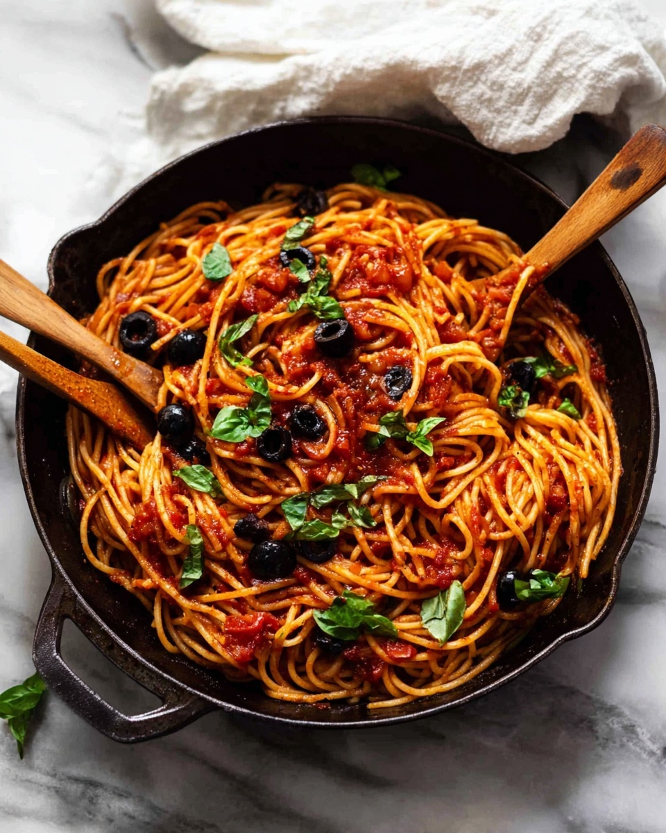 A white bowl filled with three layers of spaghetti coated in bright red tomato sauce, mixed with black olives and topped with small green basil leaves scattered around. The spaghetti strands are twisted into a neat mound in the center, with a silver fork resting on the side of the bowl. The bowl sits on a light gray cloth with a white marbled surface background, showing some green herbs lightly sprinkled nearby. In the background, there is a blurred second bowl with a similar serving of spaghetti. photo taken with an iphone --ar 4:5 --v 7