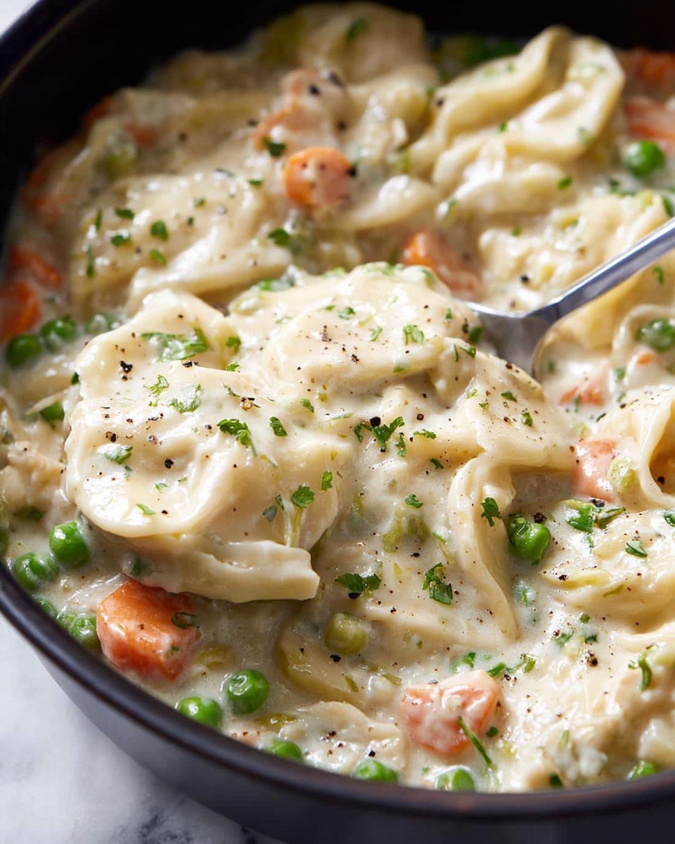 This is a close-up view of a creamy dish served in a black pot, placed on a white marbled surface. The dish has several layers: the base layer consists of a thick, pale beige creamy sauce mixed with small bright green peas and soft orange carrot cubes evenly spread throughout. On top of this layer are tender light beige pieces that look like soft flour dough or thick noodles, folded and slightly wrinkled, partially covered by the sauce. Small specks of black pepper and chopped green herbs are scattered across the dish, adding texture and color contrast. A metal spoon is digging into the thick mixture, lifting part of the dough layer from the middle of the pot. photo taken with an iphone --ar 4:5 --v 7