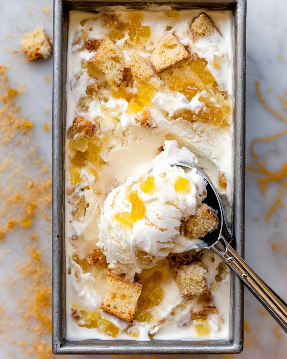 The image shows a metal loaf pan filled with creamy white ice cream mixed with light golden cake pieces scattered on top. Small chunks of translucent yellow fruit pieces are spread across the ice cream, adding texture and color contrast. A silver ice cream scoop is lifting a portion from the pan, displaying a mix of ice cream, cake, and fruit in one scoop. The pan is placed on a white marbled surface. Photo taken with an iphone --ar 4:5 --v 7