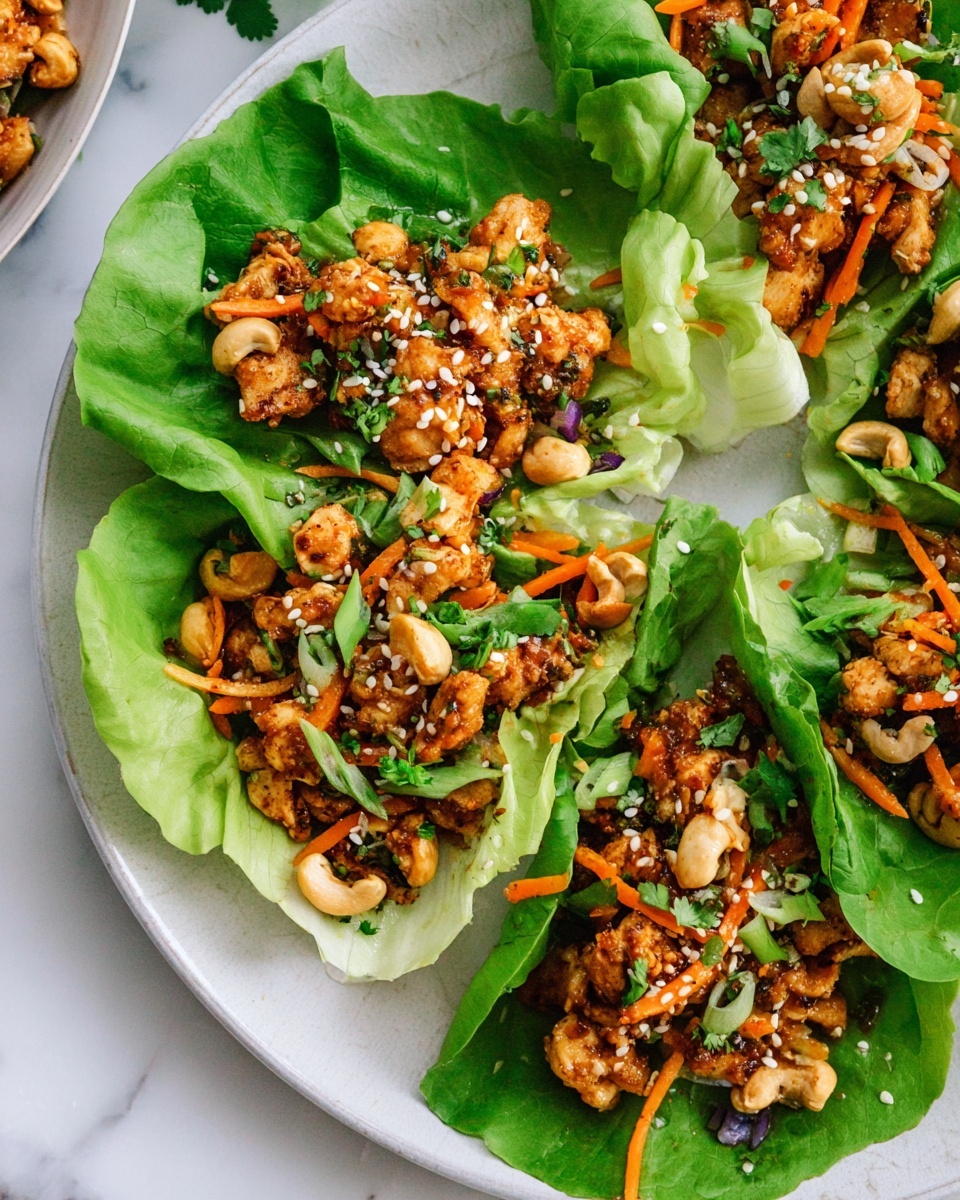 The image shows several lettuce wraps on a white plate placed on a white marbled surface. Each wrap has one large bright green leaf as the base, holding a mix of small pieces of cooked golden-brown chicken, thin orange carrot strips, and cashew nuts. The topping is sprinkled with white sesame seeds and small bits of chopped green onions and cilantro. The colors contrast well, with the fresh green lettuce leaves cradling the warm, textured filling. Photo taken with an iphone --ar 4:5 --v 7