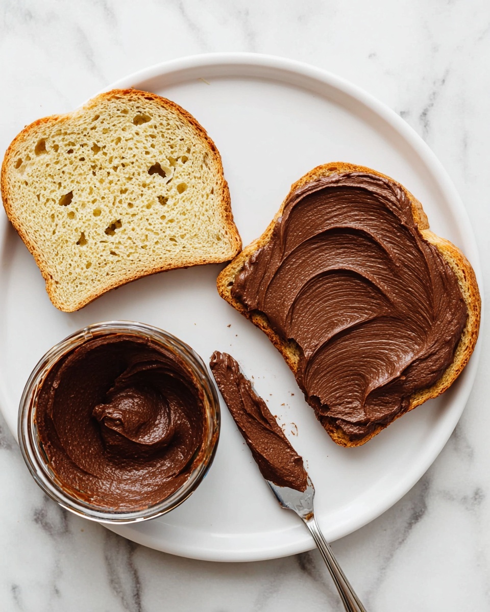 The image shows a white plate on a white marbled surface with two slices of bread. One slice is plain and positioned at the bottom left, light brown with visible holes and texture. The other slice is at the top right, covered with a thick layer of smooth, dark brown chocolate spread that has soft swirled patterns. A knife with some chocolate spread on it rests near the bottom right of the plate. Next to the plate, on the white marbled surface, is an open glass jar filled with the same dark chocolate spread, showing swirled texture on top. Photo taken with an iphone --ar 4:5 --v 7