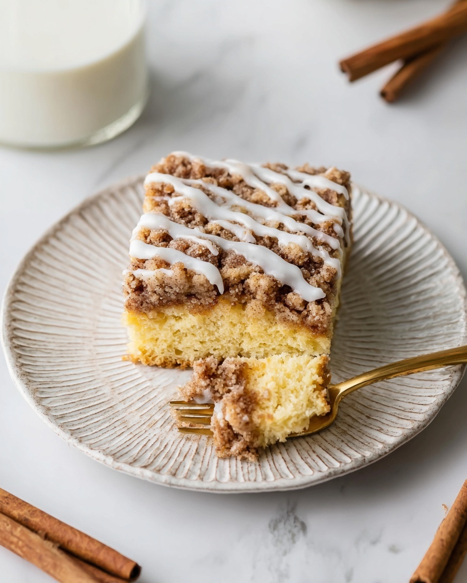 A square piece of crumb cake sits on a white plate with a textured edge, showing two main layers: a light yellow cake base and a thick, crumbly brown topping with a rough texture, drizzled with white icing in thin lines across the top. Next to the cake on the plate is a small fork holding a single bite, revealing the soft, crumbly inside with a light yellow color and a thin layer of cinnamon filling. The plate rests on a white marbled surface, and part of a glass of milk and cinnamon sticks appear in the background. Photo taken with an iphone --ar 4:5 --v 7