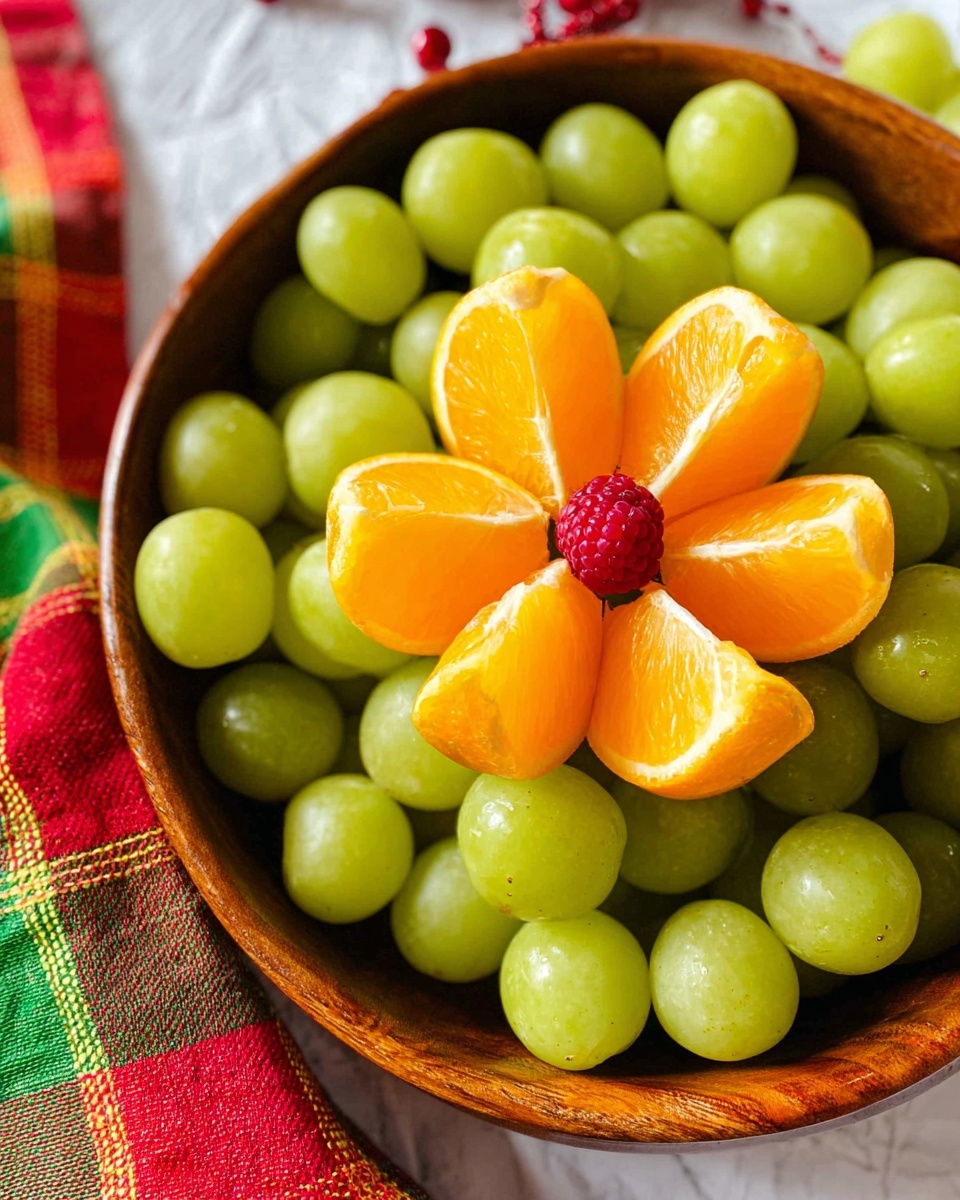A round wooden bowl filled with green grapes covers most of the space. In the center front, there is an orange cut into six thick wedges arranged in a circular flower shape with a bright red raspberry placed in the middle of the orange slices. The bowl is placed on a white marbled surface with a red, green, and yellow checkered cloth partly visible on the left side. Photo taken with an iphone --ar 4:5 --v 7