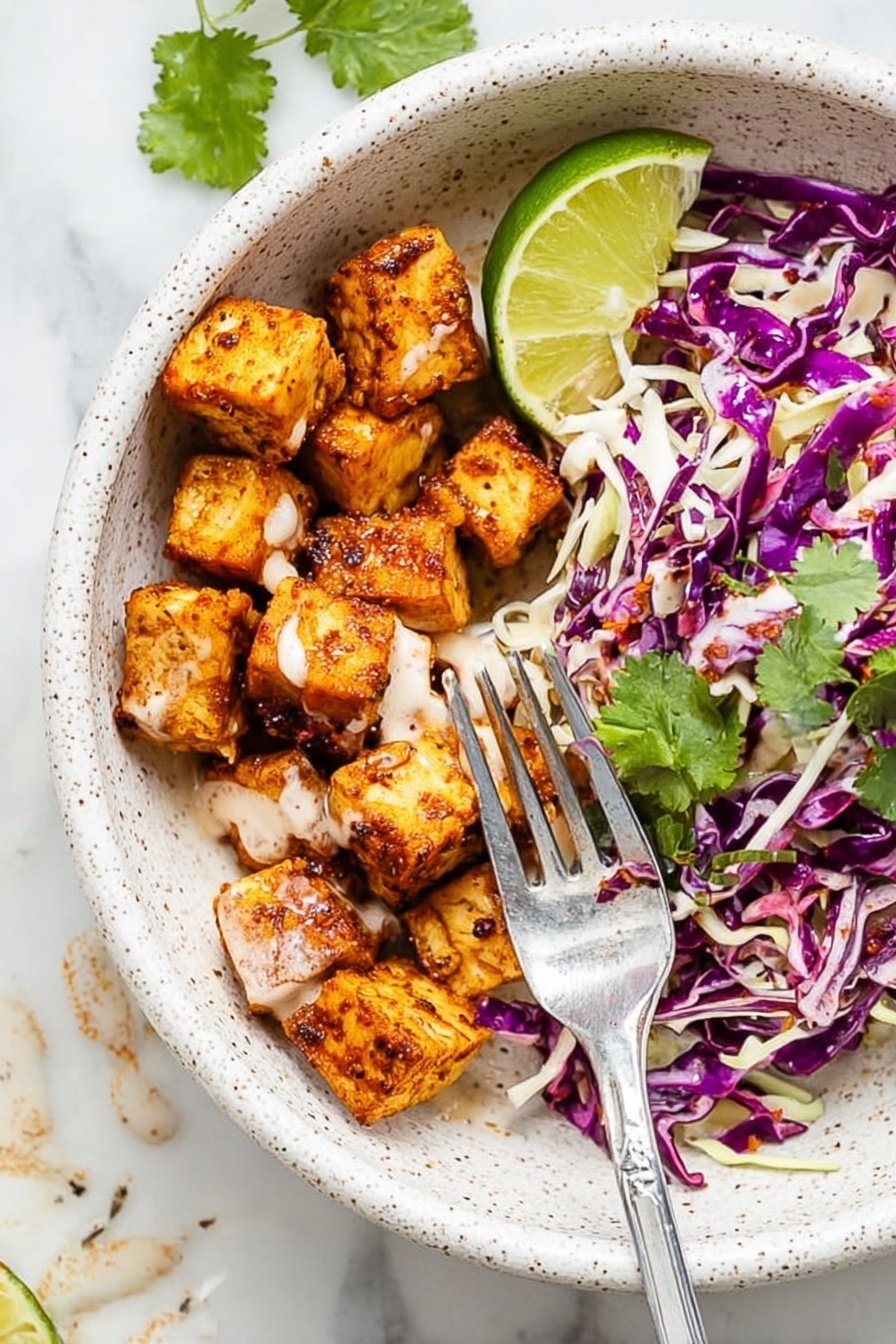 The image shows a white speckled bowl with two main layers: on one side, there are small, golden-brown seasoned cubes with a smooth light sauce drizzled over them, and on the other side, there is a mix of shredded purple and white cabbage with some green cilantro leaves scattered on top. A wedge of bright green lime sits at the edge of the bowl. A silver fork is placed inside, resting on the bowl’s edge and touching some of the cubes. The bowl is on a white marbled surface with some sauce drops visible nearby. Photo taken with an iphone --ar 2:3 --v 7 - Fish Taco Bowl with Spicy Mayo, Fish Taco Bowl, Spicy Mayo Fish Bowl, Easy Fish Taco Bowl, Healthy Fish Taco Bowl