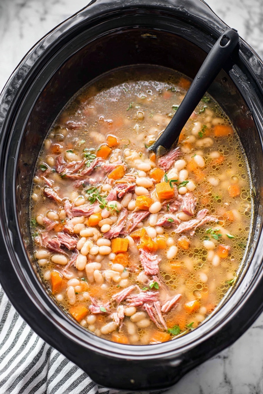 A large black slow cooker filled with a stew that has several layers and textures. The base layer shows a light brown broth with small bubbles of oil floating on top. Floating in the broth are many small, soft white beans, many small orange carrot cubes, and small bits of translucent onions. There are also shredded pieces of pinkish-brown cooked meat spread evenly throughout. Small green herbs are scattered on top, adding a fresh touch. A black spoon is partially submerged on the left side, resting inside the slow cooker. The slow cooker sits on a white marbled surface with a striped cloth partially visible below. Photo taken with an iphone --ar 2:3 --v 7 - Hearty Ham and Bean Soup, ham and bean soup, easy ham bean soup, comforting ham and bean stew, homemade ham and bean hearty soup