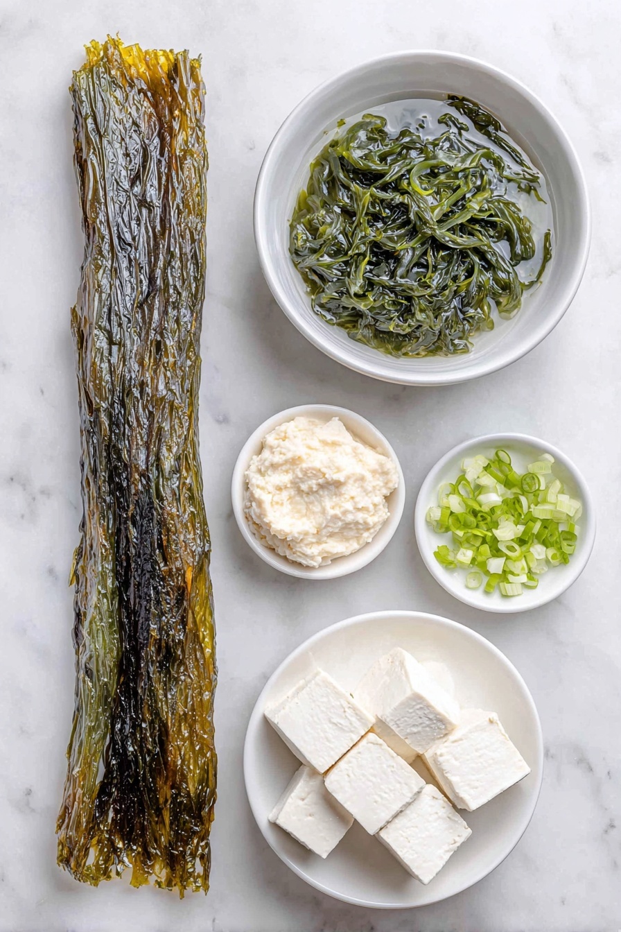 Flat lay of a long dark green fresh kombu seaweed strip, a small white ceramic bowl filled with clear water, a small white ceramic bowl holding rehydrated dark green wakame seaweed, a small white ceramic bowl with smooth pale beige white miso paste, a small pile of freshly chopped bright green onion pieces, a neat arrangement of soft white silken tofu cubes, a small white ceramic bowl filled with dark amber tamari soy sauce, placed on a clean white marble surface, soft natural light, photo taken with an iPhone, professional food photography style, fresh ingredients, white ceramic bowls, no bottles, no duplicates, no utensils, no packaging --ar 2:3 --v 7 --p m7354615311229779997 - Miso Soup with Tofu and Seaweed, easy miso soup recipe, healthy miso soup, tofu seaweed soup, quick Japanese soup