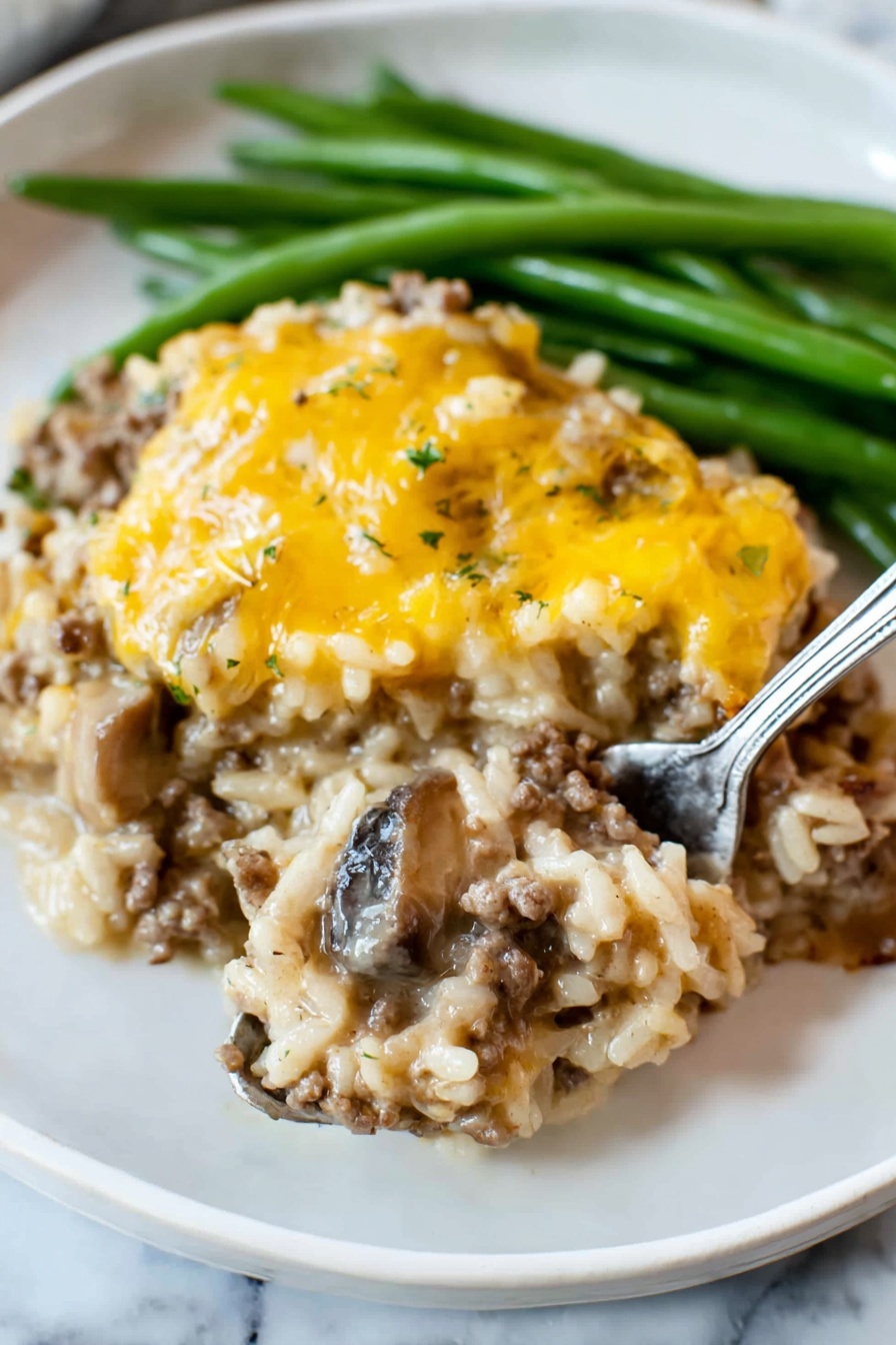 The dish shows two main layers on a white plate with green beans at the back. The bottom layer is a mix of cooked rice, ground meat, and slices of mushrooms, all combined in a creamy sauce with a light brown color and soft texture. The top layer is a covering of melted yellow cheese, unevenly spread, adding a slightly shiny and smooth look. The green beans are long and firm, bright green, placed behind the main dish. A silver fork is lifting a spoonful from the bottom layer, showing the mix of rice, meat, and mushrooms clearly. The plate is set on a white marbled surface photo taken with an iphone --ar 2:3 --v 7 - Cheesy Ground Beef and Rice Casserole, ground beef casserole, easy rice casserole, cheesy dinner recipes, hearty beef and rice dish