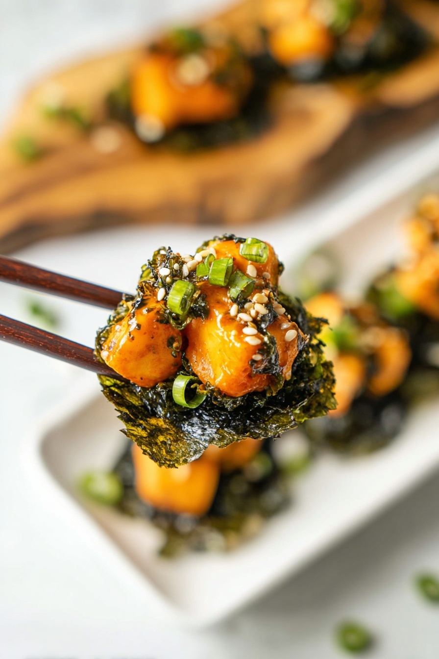 A close-up of a pair of dark brown chopsticks holding a bite-sized stack. The bottom layer is a dark green, wrinkled seaweed sheet, crisp in texture. On top, there are several pieces of light orange cooked cubes with a glossy, slightly creamy bright orange sauce covering them. The stack is garnished with small white sesame seeds and chopped green onions that add green touches to the dish. In the background, a white plate with more similar stacks rests on a white marbled surface. A blurred wooden board with more stacks is visible behind the plate. Photo taken with an iphone --ar 2:3 --v 7 - Baked Salmon Sushi Cups, sushi cups with salmon, baked salmon sushi appetizer, easy sushi cups, bite-sized sushi recipes